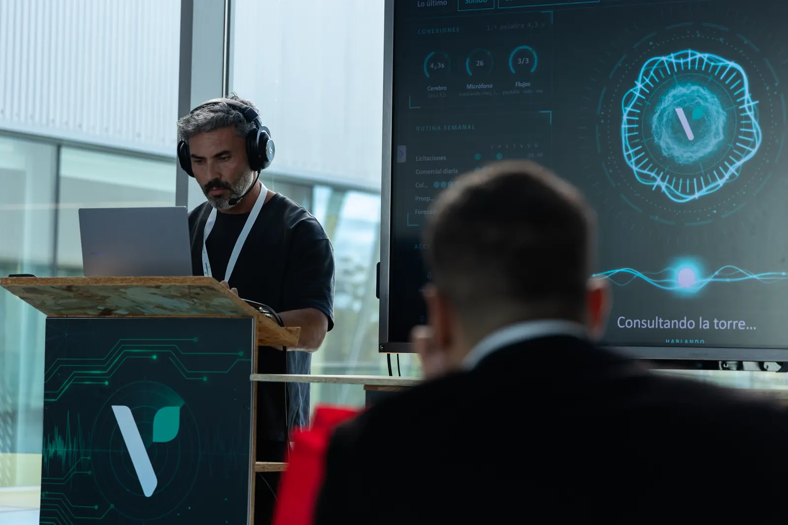 Un asistente sigue la demo en el stand de Verdtical del WGIC26 mientras la pantalla muestra «Consultando la torre…» y Daniel Guzmán trabaja en el atril.